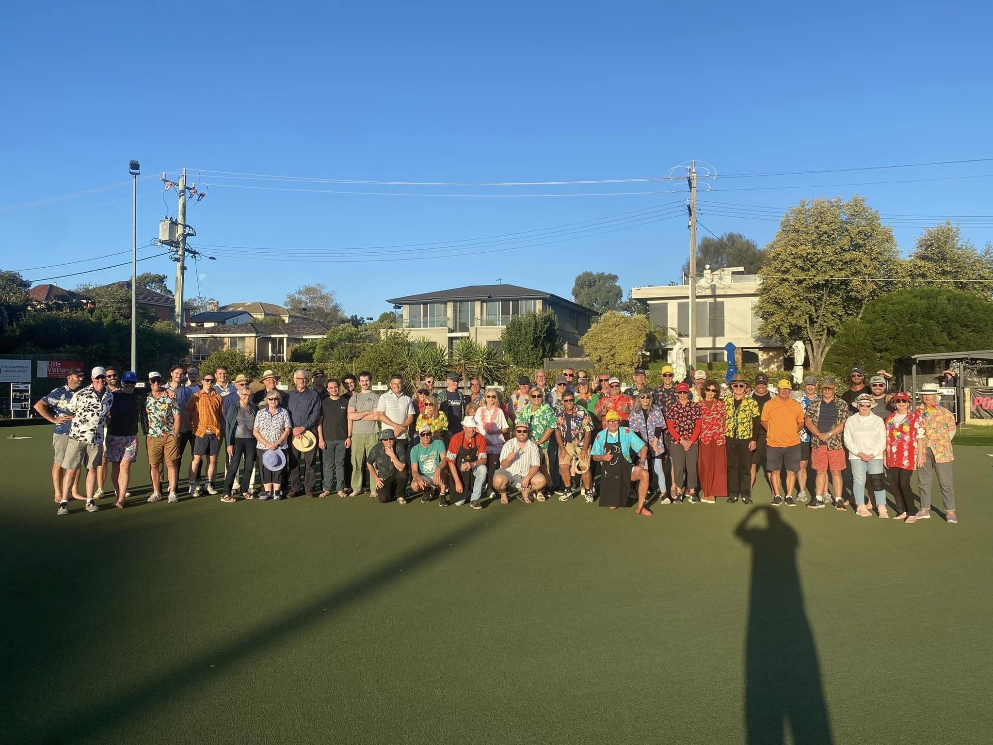 A big crowd in party shirts on the green for a barefoot bowls night