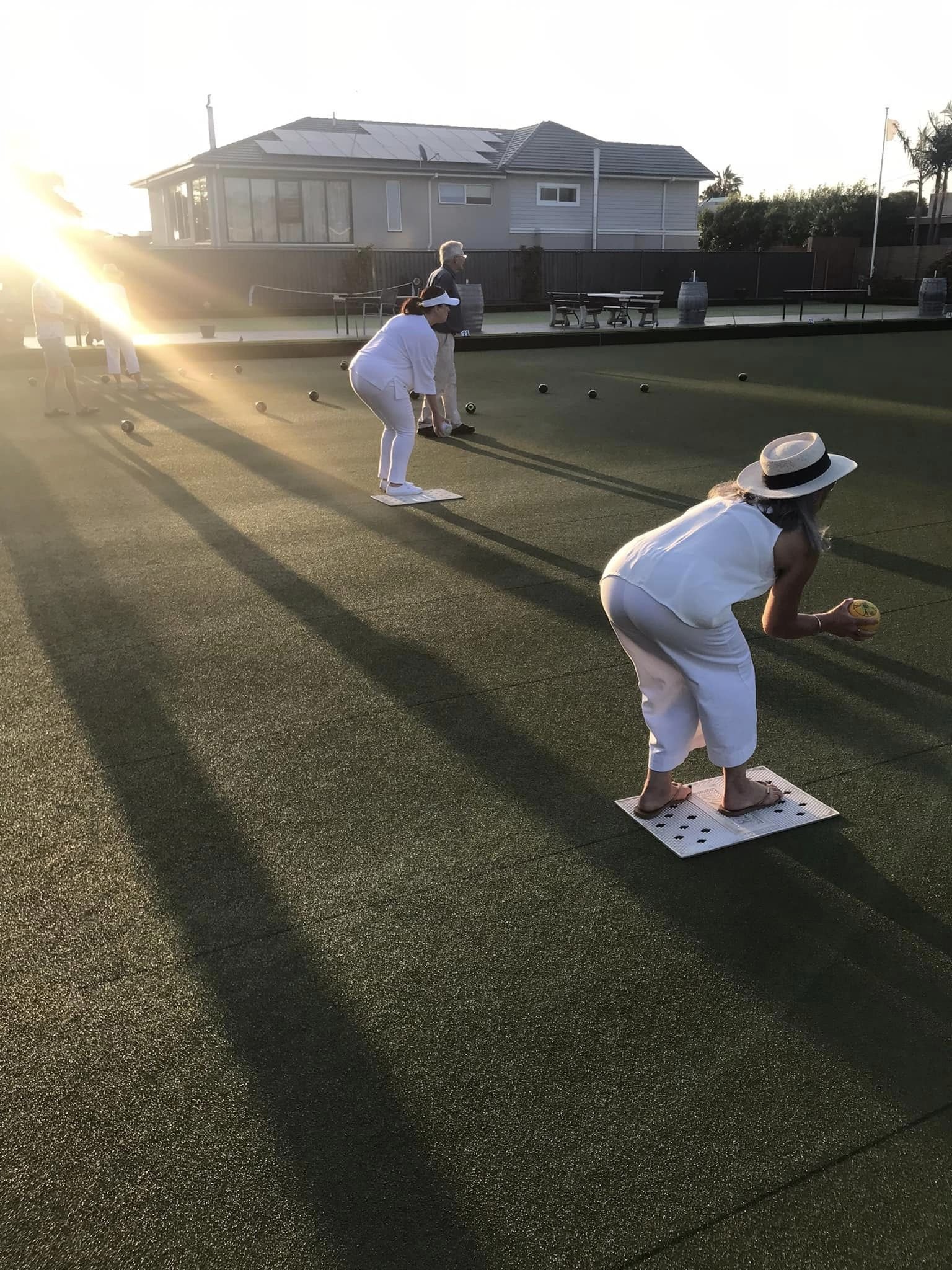 A bowler in whites delivering on the green at sunset
